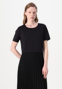 Cropped top nero con maniche corte, scollatura rotonda, abbinato a una gonna nera plissettata, caratterizzata da pieghe verticali e una texture liscia.