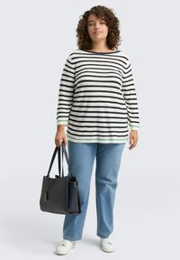 Gestreepte lange mouw top in wit en marineblauw met groene accenten, gecombineerd met lichtblauwe jeans en een zwarte tote bag. Witte sneakers maken de outfit af.