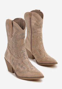 Bottes de cowboy en suède beige avec des coutures décoratives en strass, bout pointu et talon empilé, dotées d'une fermeture éclair sur le côté pour un enfilage facile.