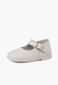 Zapato Mary Jane de cuero blanco con una correa en el tobillo, detalles de borde en forma de pico, punta redondeada y suela plana de goma. Textura suave en toda su superficie.