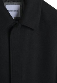 Cappotto lungo di lana nera con colletto a punta, superficie testurizzata e un'etichetta con la scritta "ANTONY MORATO" cucita all'interno del collo.