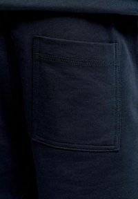 Tissu bleu marine foncé en gros plan montrant une poche plaquée rectangulaire avec des coutures visibles sur un vêtement.