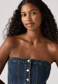 Haut sans bretelles en denim avec une coupe ajustée, comportant cinq boutons à l'avant, des coutures visibles, et une couleur bleu foncé avec un tissu texturé.