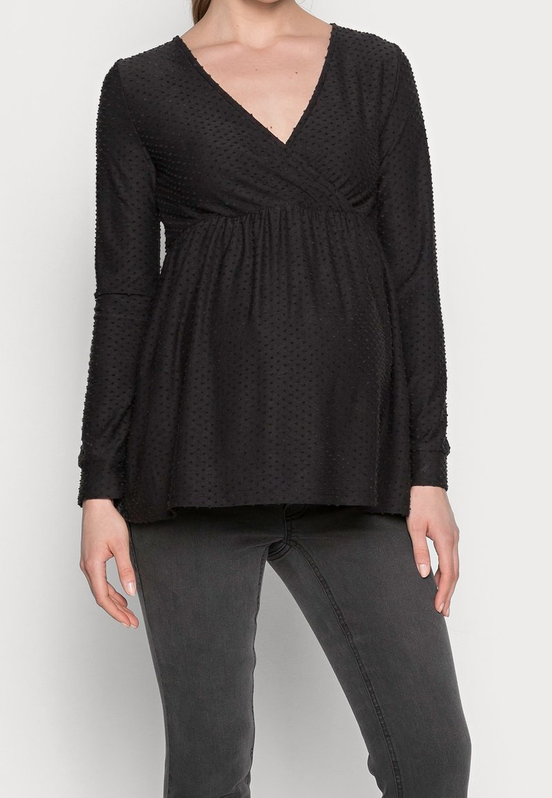 Černý těhotenský top s dlouhým rukávem a výstřihem do V, se strukturou bodových vzorů a nařaseným empírovým pasem, doplněný tmavě šedými džíny.