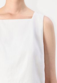 White sleeveless top with a square neckline, made of textured fabric. Features clean lines and minimalistic design.