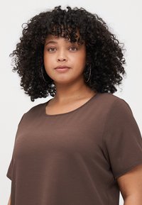 Brown short-sleeve top in a textured fabric with a round neckline, featuring relaxed fit and smooth seams for a comfortable wear.