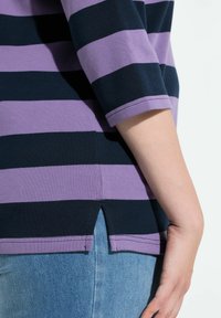 Stribet top i lilla og marineblå bomuld med trekvartærmer og sideslids for bevægelsesfrihed.