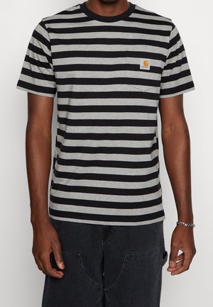Person trägt ein schwarz-grau gestreiftes T-Shirt mit einer Brusttasche vorne und dunkle Hosen.