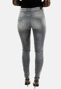 Jeans de denim gris ajustados con un acabado desgastado, cinco bolsillos y detalles de costura. Combinados con zapatos de tacón negro.