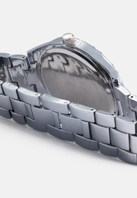 Stainless steel wristwatch with a polished silver-tone metal bracelet, round case, and a prominent crown. The back shows engraved details.
