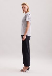 Grå bomuld T-shirt med korte ærmer, kombineret med sorte skræddersyede bukser og sorte sandaler med hæl, vist fra siden.