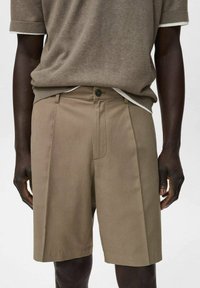 Pantaloni scurți pliati khaki dintr-un material ușor, cu închidere cu nasture și buzunare laterale, asortați cu un top scurt cu mânecă.