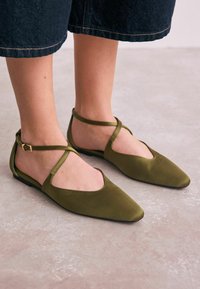 Bailarinas de ante verde con punta afilada, correas en el tobillo y detalles recortados. Textura suave y diseño minimalista.