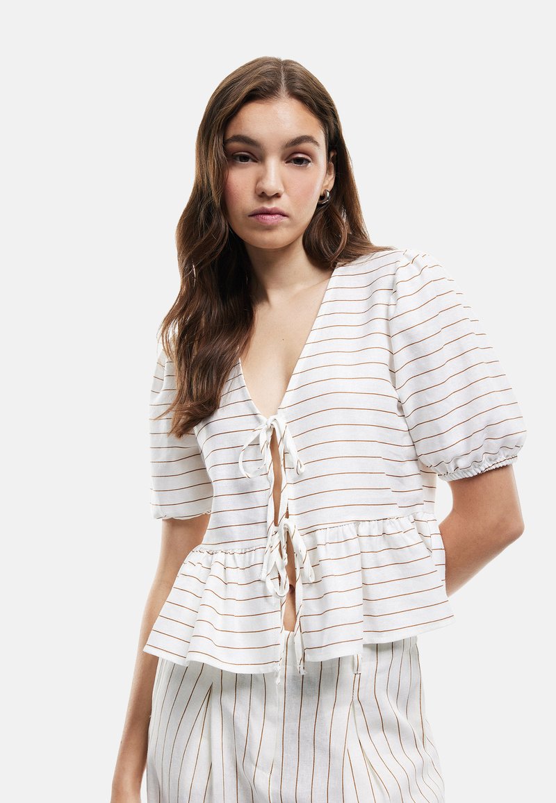 Top peplum in tessuto leggero con strisce bianche e marroni, scollatura a V profonda, chiusura a fiocco e maniche a sbuffo. Progettato per una vestibilità rilassata.