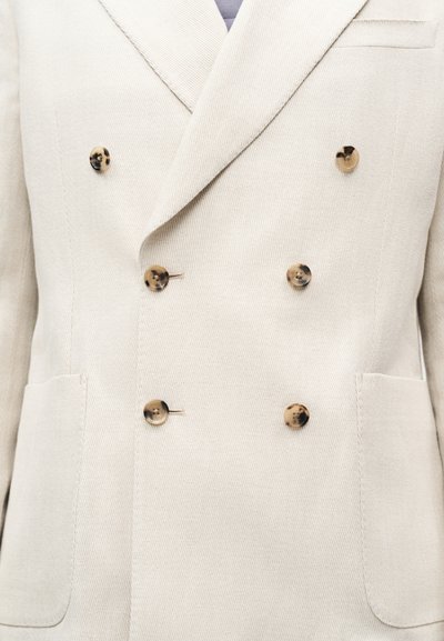 Blazer croisé couleur ivoire clair avec six boutons en écaille et deux poches plaquées devant sur un tissu texturé.