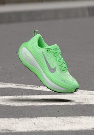 Αθλητικό παπούτσι Nike ZoomX σε νέον πράσινο χρώμα στον αέρα πάνω από μια υφασμένη γκρίζα ασφάλτινη επιφάνεια με λευκές σημάνσεις.
