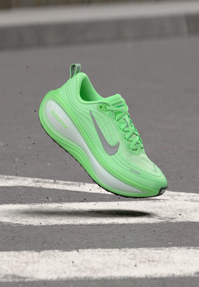 Αθλητικό παπούτσι Nike ZoomX σε νέον πράσινο χρώμα στον αέρα πάνω από μια υφασμένη γκρίζα ασφάλτινη επιφάνεια με λευκές σημάνσεις.
