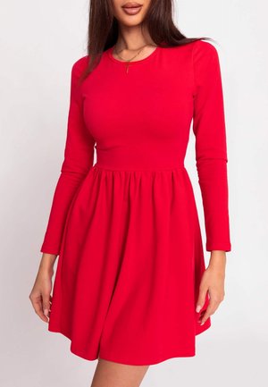 Frau trägt ein leuchtend rotes langärmeliges Kleid mit taillierter Passform und ausgestelltem Rock, accessoriert mit einer goldenen Kreuzkette.