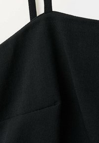 Gros plan d’un tissu noir avec une fine sangle et une surface lisse, légèrement texturée, montrant les détails des coutures.
