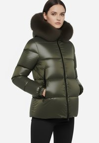 Giacca puffa verde oliva con colletto in pelliccia scura staccabile, chiusura con zip e polsini elastici. Materiale liscio e lucido con design trapuntato.