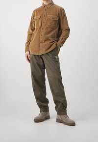 Brun kordfløjlsjakke med knaplukning og to brystlommer, kombineret med løstsiddende olivengrønne cargobukser og beige ankelstøvler.