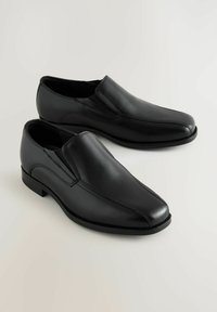 Zapatos negros tipo mocasín hechos de cuero suave con un diseño de punta, detalles de costura sutiles y un tacón bajo para un uso fácil.