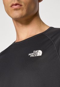 T-shirt de desempenho preto com um acabamento texturado, apresentando um logótipo branco da "THE NORTH FACE" na área do peito esquerdo. Gola redonda.