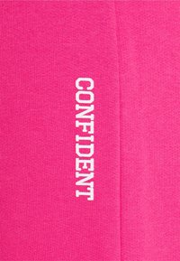 Růžové legíny z jemné tkaniny s hladkou texturou, na boku s výrazným bílým nápisem "CONFIDENT".