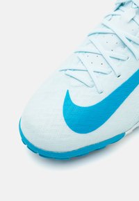 Zapatilla deportiva de color azul claro con una superficie texturizada, que presenta un gran swoosh de Nike en color turquesa y cordones planos. Punta redonda y suela de goma.