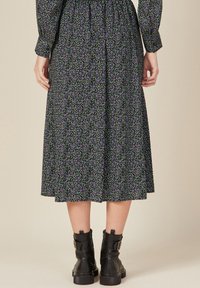 Blumen-Midi-Kleid mit schwarzem Hintergrund, verziert mit lila und weißen Blumenmustern. Stylisch kombiniert mit schwarzen Knöchelstiefeln, mit gerafftem Taillenbund und langen Ärmeln.