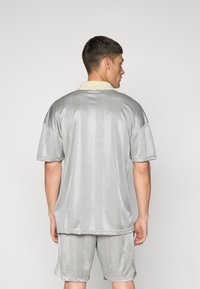 Grå t-skjorte med korte ermer og lysfarget krage samt mønstrete tekstur. Kombinert med matchende grå shorts som har en avslappet passform.