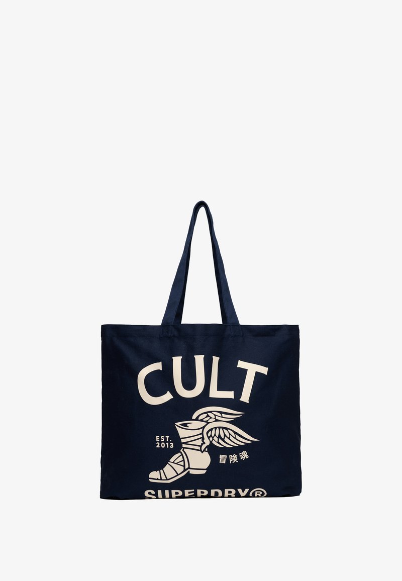 Granatowa torba płócienna z dwiema rączkami, z dużym białym napisem "CULT" i grafiką skrzydlatej boot w stylu vintage, założona w 2013 roku.