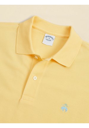 Polo di colore giallo chiaro con colletto piegato, due bottoni e piccolo logo ricamato blu sul petto.