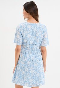 Helles blaues Blumenmusterkleid mit kurzen Ärmeln, gerafftem Bund und knieumspielendem Saum. Der Stoff hat ein strukturiertes, leichtes Aussehen.