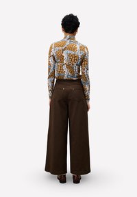 Chemise à manches longues à motifs marron associée à un pantalon taille haute, jambes larges, de couleur marron foncé. Le pantalon comporte des poches arrière et des coutures discrètes.