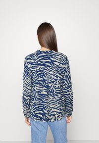 Langarmshirt in Marineblau und Creme mit einem Tigermuster, mit rundem Halsausschnitt und gerafftem Detail im Rückenteil. Der Stoff wirkt leicht.