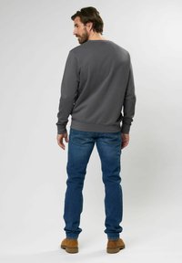 Grijze sweatshirt met een ronde hals, geribbelde manchetten en zoom, gecombineerd met blauwe spijkerbroek en bruine laarzen, gezien vanaf de achterkant. Minimale details.