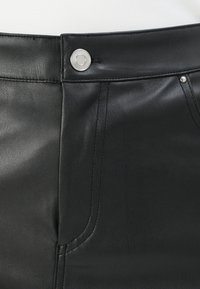 Close-up van zwarte leren broek met een zilveren knoop, voorzak en gedetailleerde stiksels op de tailleband en rand van de zak.