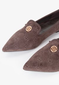 Ballerine in suede marrone con punte appuntite, caratterizzate da motivi geometrici ricamati e un bottone decorativo in tonalità oro su ciascuna scarpa.