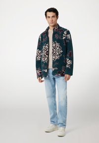 Tamsiai mėlynas fliso džemperis su baltu ir bordo gėlių raštu, su stovinčiu apykakle, užtrauktuku priekyje, derinamas su šviesiai mėlynomis džinsais ir baltais sportbačiais.