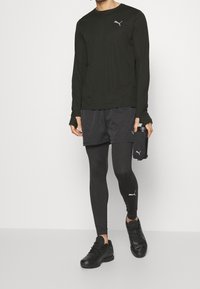 Svart långärmad prestationsskjorta, svarta shorts, svarta leggings och svarta sneakers med en silver Puma-logotyp. Enkelt, atletiskt design.