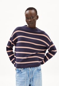 Marineblauw en roze gestreepte trui met een bootnek en verlaagde schouders, gecombineerd met lichtblauwe denim jeans.