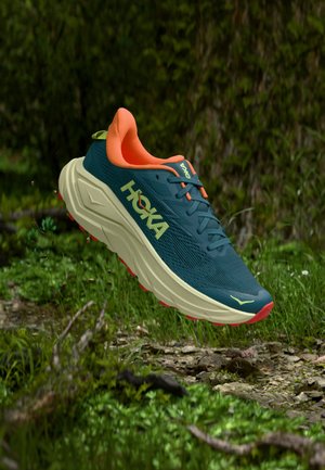 Chaussure de course HOKA en bleu sarcelle avec des accents orange. Elle présente une tige texturée, un design léger, une semelle intermédiaire épaisse de couleur crème et une semelle extérieure rouge.