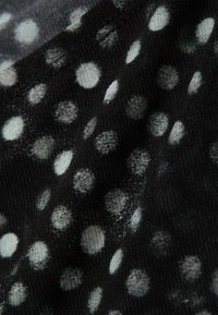 Μαύρο ύφασμα με υφή που διαθέτει λευκές και ανοιχτό γκρι κουκκίδες διαφόρων μεγεθών, δημιουργώντας ένα στίγμα μοτίβου.