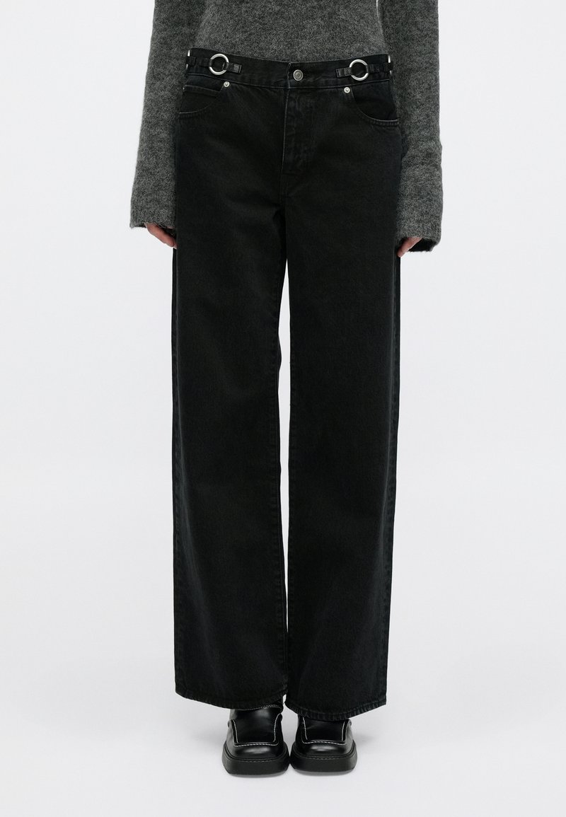 Fekete, széles szárú, magas derekú farmernadrág fém kör díszítéssel, klasszikus zsebekkel és puha farmer anyaggal. Feketecipővel párosítva.