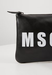 Pochette zippée en cuir noir avec de grandes lettres blanches "MSC" visibles sur le devant, sur fond blanc uni.