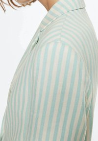 Gestreifte Bluse in Hellblau und Creme, mit Kragen und Knopfdetails. Der Stoff wirkt glatt und hat eine weiche Textur.