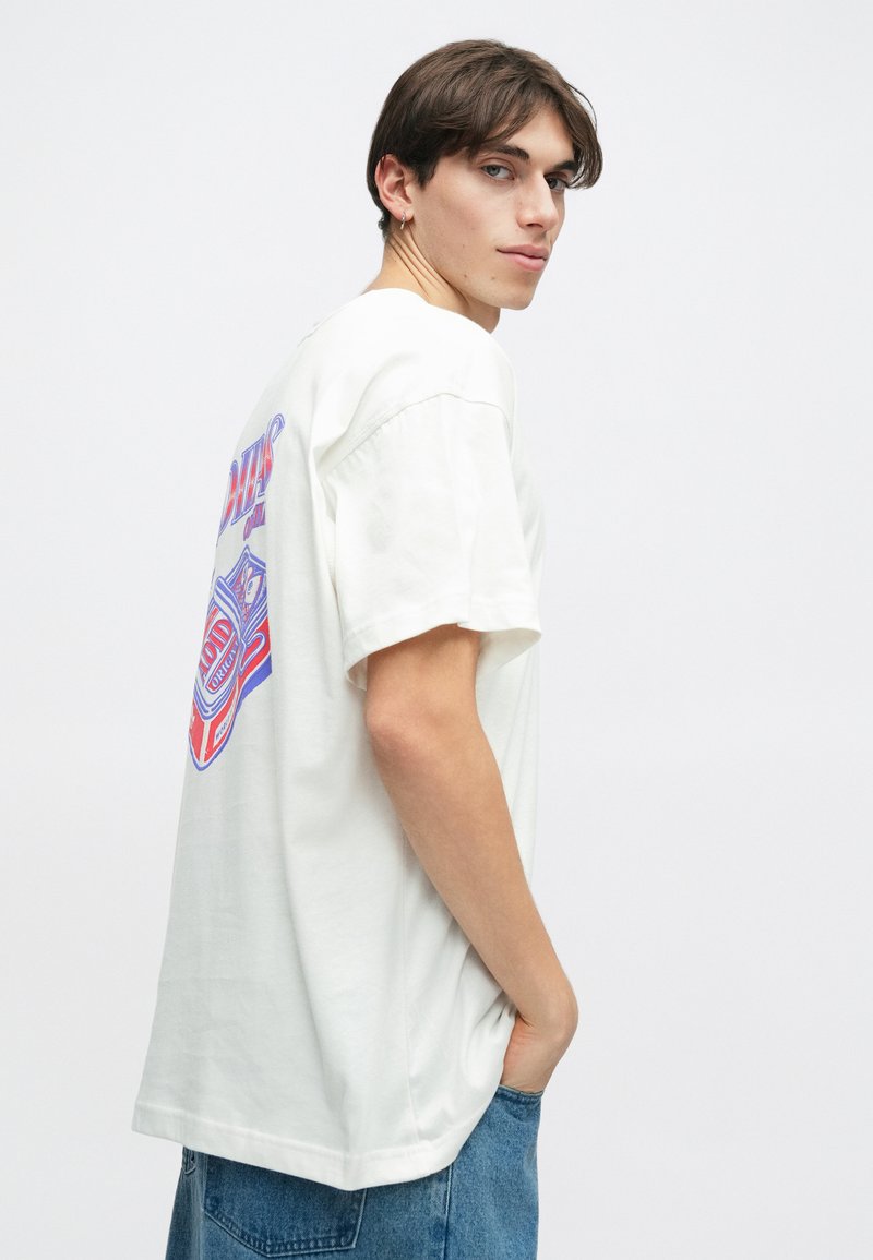 White cotton t-shirt featuring a graphic print on the back in red and blue, short sleeves, and a relaxed fit with a straight hem.