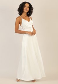 Weißes Satin-Maxikleid mit tailliertem Oberteil, tiefem V-Ausschnitt und dünnen Trägern. Der fließende Rock fällt bis zum Boden. Elegantes und nahtloses Design.