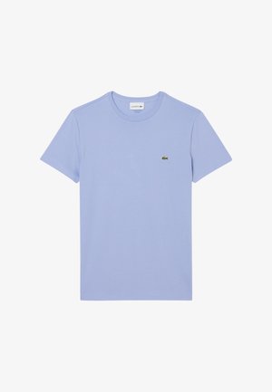 Camiseta de manga corta azul claro con un pequeño logo de cocodrilo verde de Lacoste en el lado izquierdo del pecho. Diseño simple y casual.